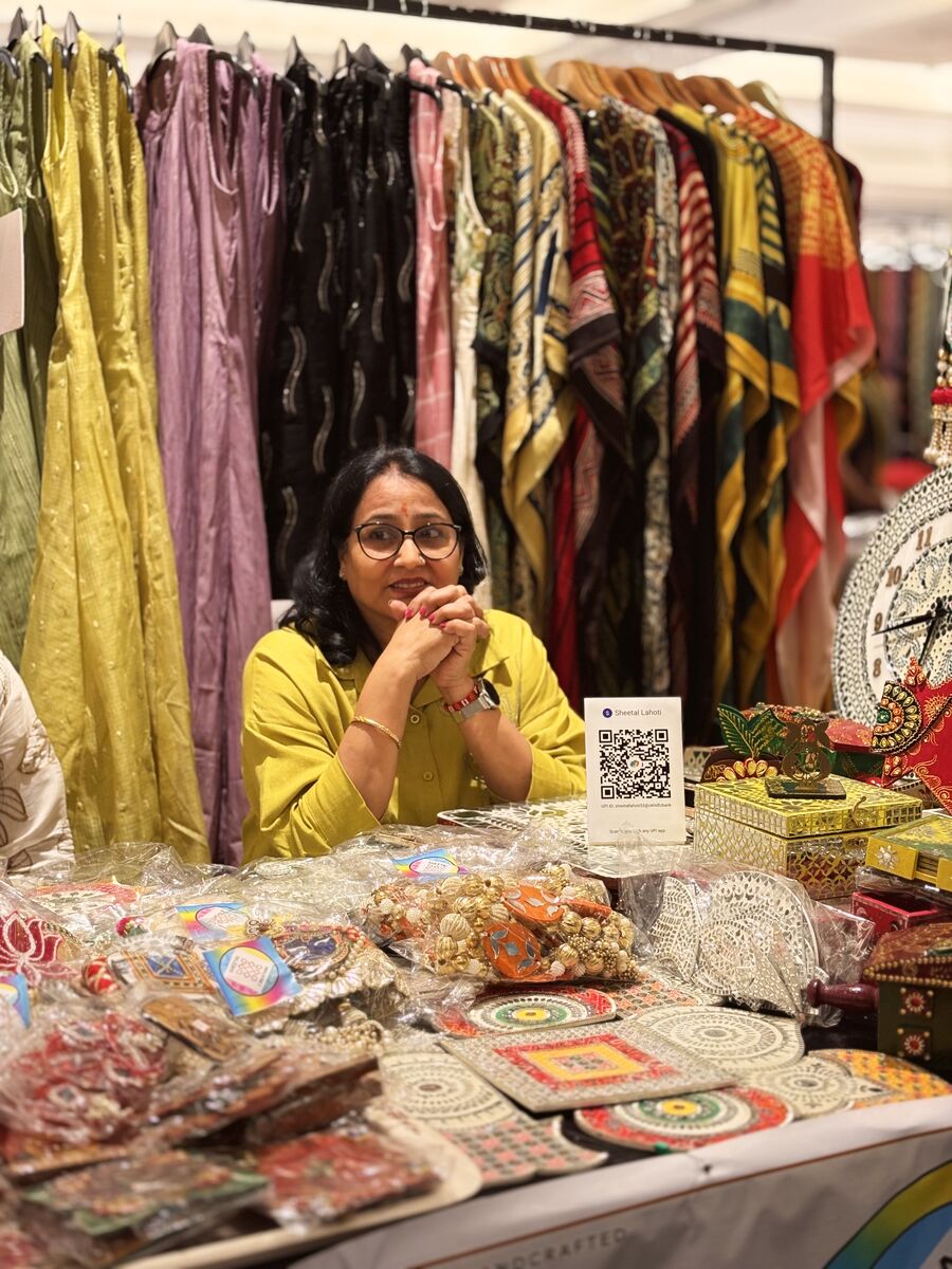 A vendor smiling behind her stall of handcrafted decor and printed kaftans